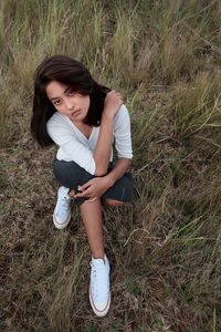 High angle portrait of beautiful young woman sitting on grassy field