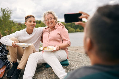 Man photographing grandson and grandmother with meal on rock during picnic