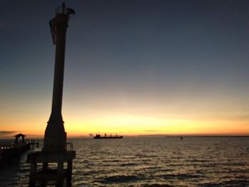 Silhouette statue by sea against sky during sunset