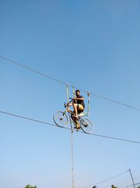 Low angle view of man riding bicycle on rope against clear blue sky