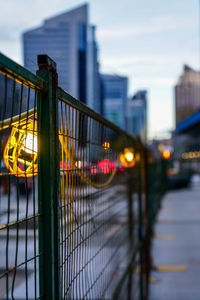 Illuminated city against sky seen through fence
