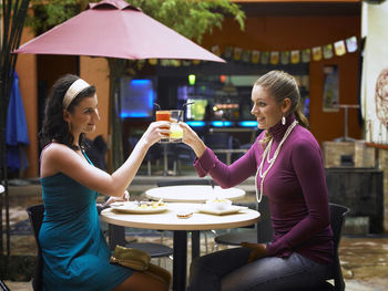 Cheerful female friends toasting drinks while sitting at outdoor cafe