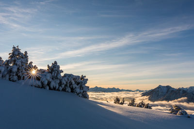 Snow covered landscape against sky during sunset