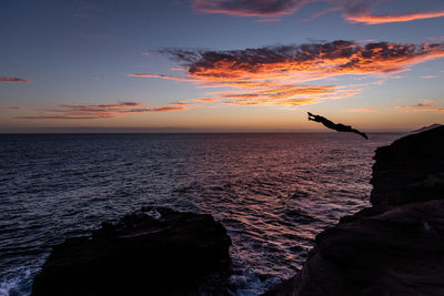 Cliff diver over the ocean at sunset in hawaii