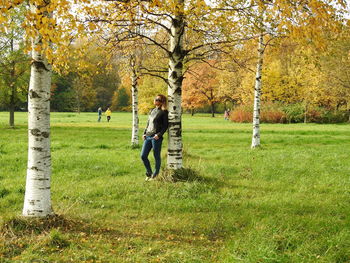 Full length of woman standing on grass against tree trunk