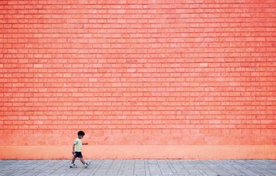 Full length of boy walking on sidewalk against wall