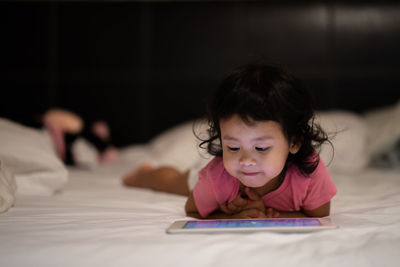Girl using digital tablet while lying on bed 