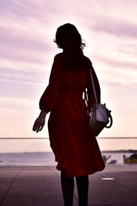 Rear view of woman standing against sky during sunset