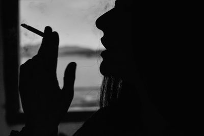 Close-up of silhouette young woman smoking cigarette in darkroom