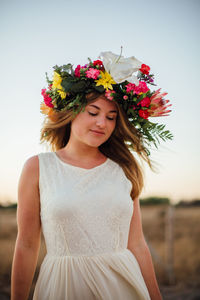 Woman wearing flowers on field against sky