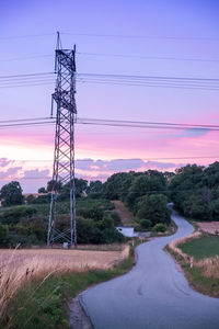 Electricity pylon by road against sky during sunset