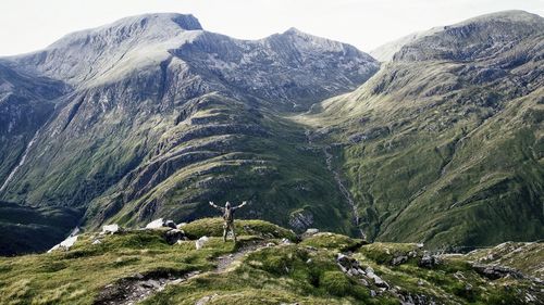 Rear view of man with arms outstretched standing against mountains