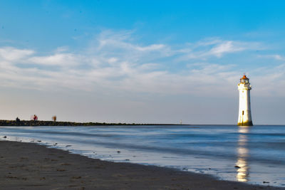 Lighthouse on beach by sea against sky