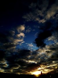 Low angle view of sunlight streaming through clouds during sunset