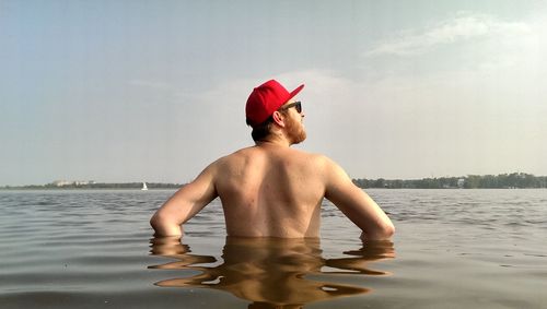 Rear view of shirtless man standing in lake against sky