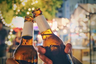 Close-up of friends toasting beer bottles at night