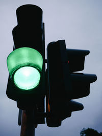 Low angle view of illuminated green road signal against sky