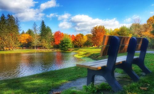 Bench in park by lake against blue sky