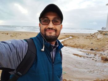 Portrait of smiling man standing at beach against sky