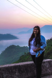 Young woman standing against sky during sunset