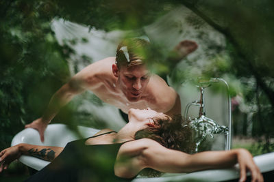 Midsection of shirtless man holding water while sitting outdoors