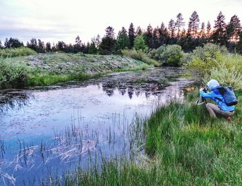 Man sitting on field by lake against sky