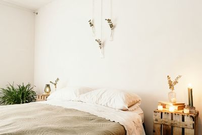 Light bedroom with minimalist interior including comfortable bed and wooden furniture with boho decoration on white wall