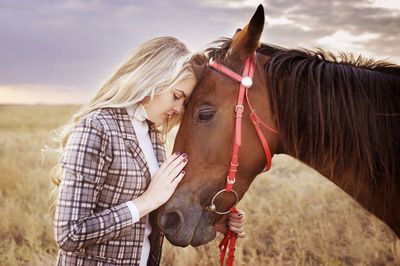 Profile view of young woman standing face to face with horse on field