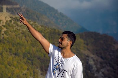 Young man gesturing peace sign while standing against mountains