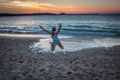 Full length of woman jumping at beach against sky during sunset