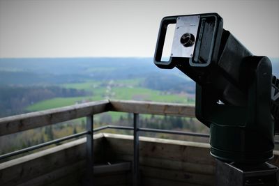 Close-up of coin-operated binoculars by railing against sky