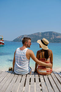 Rear view of people sitting on shore against clear sky