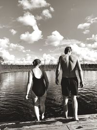 Rear view of friends standing by lake against sky