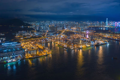 Illuminated buildings by river against sky at night