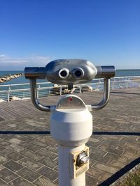 Close-up of coin-operated binoculars by sea against sky