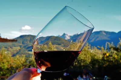 Cropped hand holding wineglass against blue sky