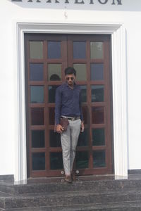 Portrait of young man standing against window of building