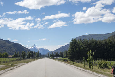 Empty road along trees and mountains against sky