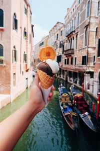 Cropped hand holding ice cream cone against canal in city