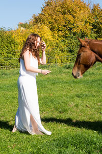 Side view of young woman with horse standing on grassy field against trees