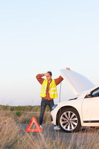 Side view of man standing by car against clear sky