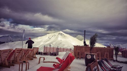 Rear view of man at observation point by snow covered mountain against cloudy sky