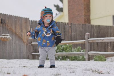 A young boy plays in the snow while wearing only one glove.