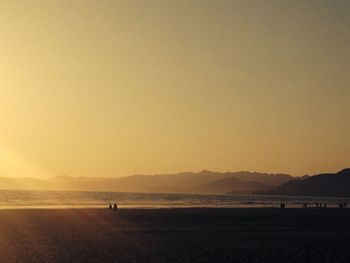 People at beach against clear sky during sunset