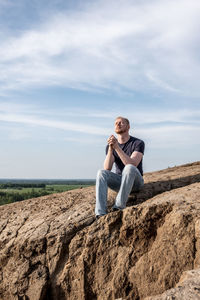 Side view of woman sitting on rock at beach against sky