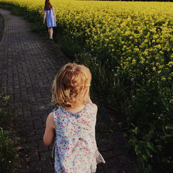 Rear view of sisters walking on footpath amidst plants