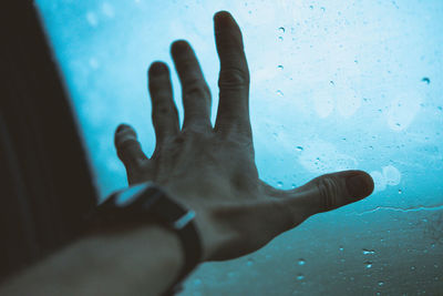 Cropped hand on man touching wet window in car