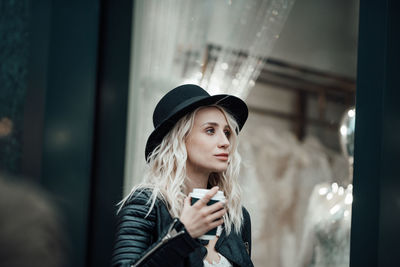 Portrait of young woman using mobile phone at window