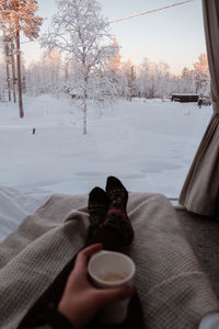 Low section of person with coffee in tent on snow covered trees during winter