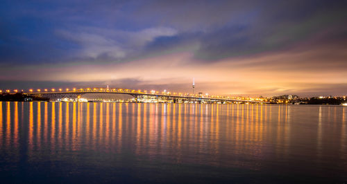 Illuminated bridge over sea against sky at sunset